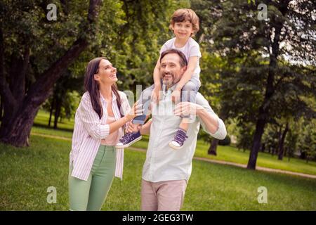 Foto von niedlichen charmanten preteen junge Mädchen Mutter Vater gekleidet casual Outfit Wandern zurück lächelnd außerhalb Stadtpark reiten Stockfoto