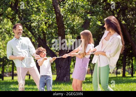 Foto von süß funky preteen junge Mädchen Mutter Vater gekleidet casual Outfit ziehen Seil mit Spaß zu Fuß lächelnd außerhalb Stadtpark Stockfoto