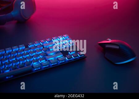 Blickfeld der blauen hinterleuchteten Tastatur und Maus auf dem Schreibtisch. Violettes Licht von oben. Professionelle Computerspiel spielen, eSport Business und Stockfoto