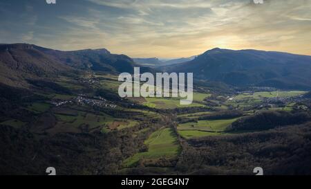 Schöner Blick auf Bergwälder und grüne Felder unter einem bewölkten Himmel bei Sonnenuntergang in Navarra, Spanien Stockfoto