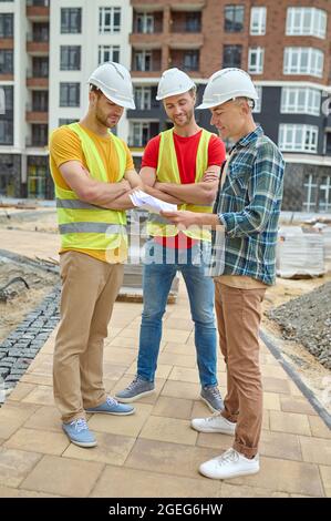 Drei Männer in Schutzhelmen analysieren technische Zeichnungen Stockfoto