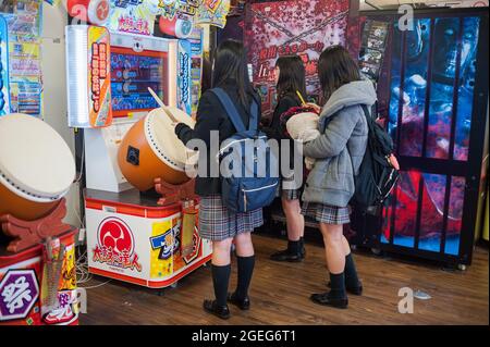 25.12.2017, Kyoto, Japan, Asien - drei japanische Schülerinnen in Schuluniform stehen vor einer Spielmaschine und spielen ein Taiko no Tatsujin. Stockfoto