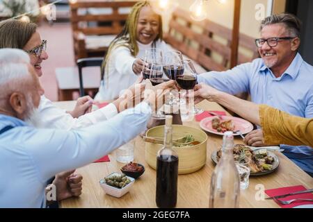 Ältere Menschen mit unterschiedlichen Rassen, die beim Abendessen auf der Terrasse mit Wein jubeln, können sich auf die Hände konzentrieren, die Gläser halten Stockfoto