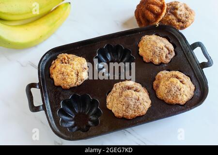 Hausgemachte Bananenmuffins in einer rustikalen, antiken Muffin-Pfanne über einer Küchenplatte. Selektiver Fokus auf den Vordergrund mit unscharfem Hintergrund. Stockfoto