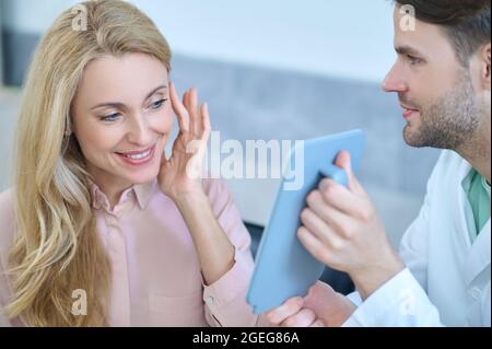 Glückliche Patientin, die ihre Spiegelung im Glas bewundert Stockfoto