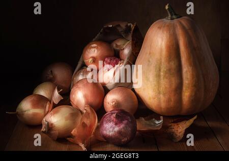 Zwiebeln in einem Stoffbeutel und Kürbis auf dunklem Holzhintergrund Stockfoto