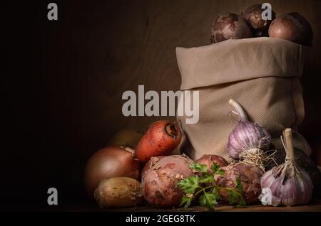 Kartoffeln in einem Stoffbeutel und anderes Gemüse in einem Rustikaler Stil auf einem dunklen Holzhintergrund Stockfoto