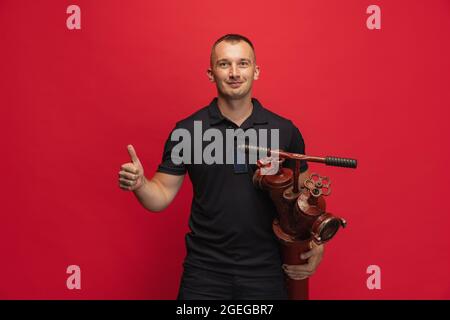 Porträt eines jungen lächelnden Mannes mit einem Hydranten vor rotem Hintergrund. Stockfoto