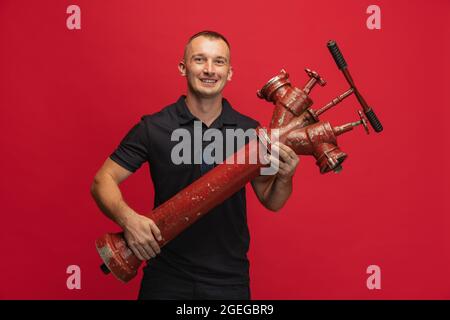 Porträt eines jungen lächelnden Mannes mit einem Hydranten vor rotem Hintergrund. Stockfoto