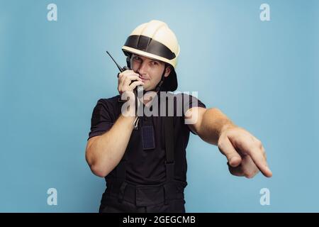 Ein junger männlicher Feuerwehrmann in Uniform, der die Anweisungen gibt, koordiniert die Arbeit des Teams. Stockfoto