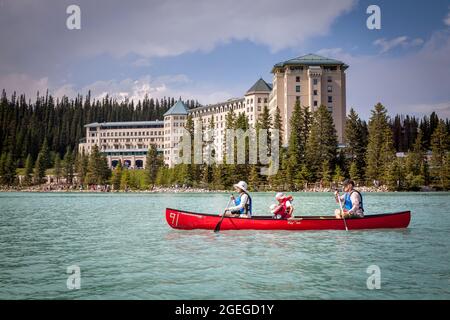 Blick auf Touristen auf einem roten Kanu in Lake Louise vor dem Hintergrund des Fairmont Hotels in der Banff National Park Region von Alberta. Stockfoto