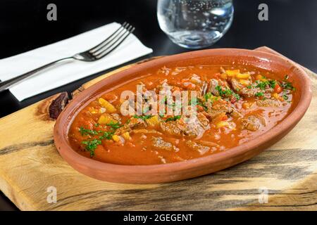 Fleisch in weißer Kasserolle auf schwarzem Steintisch sautiert Stockfoto