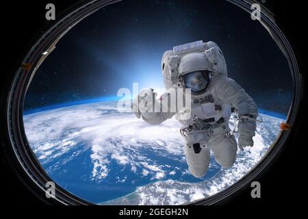 Astronaut im Weltraum aus dem Bullauge auf dem Hintergrund der Erde. Elemente dieses Bildes, die von der NASA eingerichtet wurden. Stockfoto