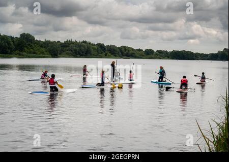 Whittligham Broad mit Kindern, die unter Anleitung das Paddleboard lernen, alle tragen Schwimmwesten Stockfoto