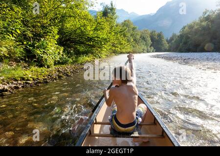 Ein Junge paddelt in einem Kanu auf dem Sava bohinjka Fluss kurz vor dem Bohinj See an einem wunderschönen Sommertag in slowenien Stockfoto