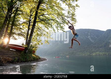 Ein Junge, der an einem wunderschönen Sommertag auf dem Bohinjsee in Slowenien von einem Baumseil springt Stockfoto