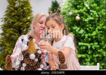 Ältere kaukasische Frau, die mit zwei Enkelinnen Tannenzapfen zu weihnachten schmückende Stockfoto