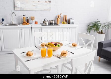 Frischer Orangensaft, leckere Pfannkuchen und Obst auf dem Tisch in der modernen Küche Stockfoto