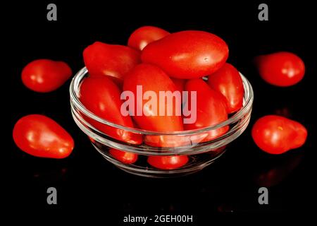 Reife rote Tomaten in Form von Erdbeeren mit Glaswaren, Nahaufnahme, isoliert auf schwarz. Stockfoto