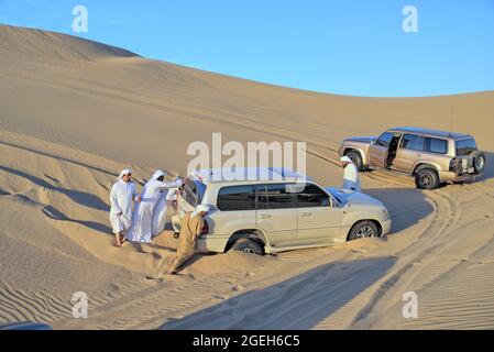 Arabische Männer schieben SUV-Auto stecken in Sand der Wüste. Stockfoto