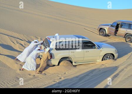 Arabische Männer schieben SUV-Auto stecken in Sand der Wüste. Stockfoto