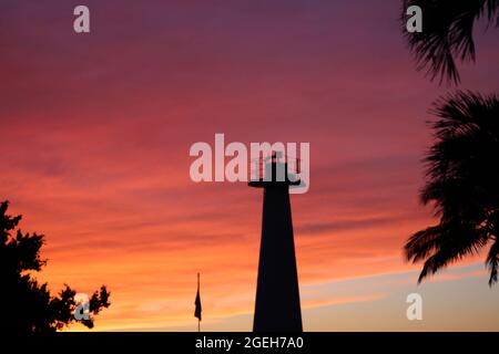 In Lahaina, Maui, Hawaii, USA, wurde ein Leuchtturm und eine Palme in der Abenddämmerung mit Rosa, Orangen und Gelbtönen vor einem atemberaubenden Himmel umragt Stockfoto