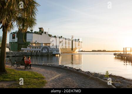 Ein riesiges Frachtschiff, das neben einem Raddampfer auf dem Cooper River in der Innenstadt von Charleston, South Carolina, USA, festmacht Stockfoto