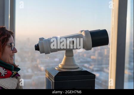 Eine Frau schaut durch ein Fernglas auf der Aussichtsplattform eines Wolkenkratzers Stockfoto