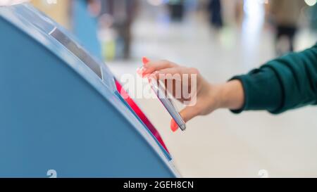 Eine gesichtslose Frau scannt den qr-Code von ihrem Smartphone aus. Ein Mädchen nutzt am Flughafen einen Self-Service-Automaten, um für einen Flug einzuchecken und Tickets auszudrucken Stockfoto