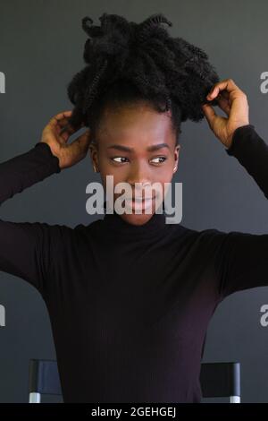 Junge afrikanerin in schwarzem Pullover auf einem Stuhl auf schwarzem Hintergrund sitzend. Stockfoto