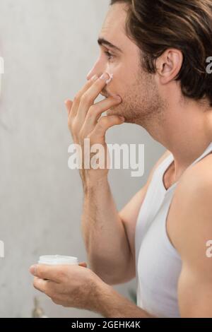 Seitenansicht des jungen Mannes, der morgens Gesichtscreme aufgibt Stockfoto