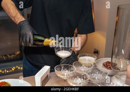 Ein Kellner in schwarzen Schutzhandschuhen gießt Champagner aus nächster Nähe. Catering. Selektiver Fokus. Stockfoto