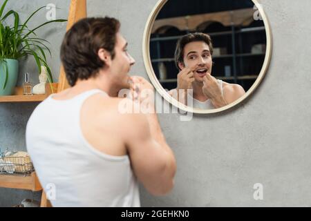 Brunette Mann in weißen Tank top Reinigung Zähne im Badezimmer in der Nähe des Spiegels Stockfoto