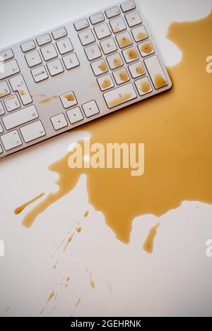 Verschüttete Tropfen schwarzen Kaffees auf einer weißen Computertastatur Stockfoto