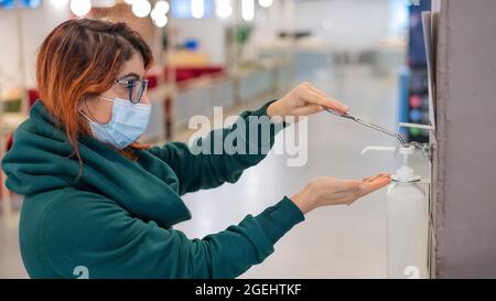 Eine Frau benutzt eine Reinigungsstation an der Wand an einem öffentlichen Ort. Nahaufnahme der weiblichen Hände, die mit Antiseptikum behandelt werden Stockfoto