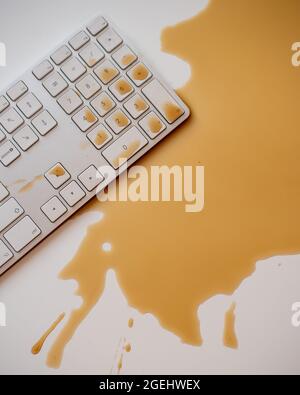 Verschüttete Tropfen schwarzen Kaffees auf einer weißen Computertastatur Stockfoto