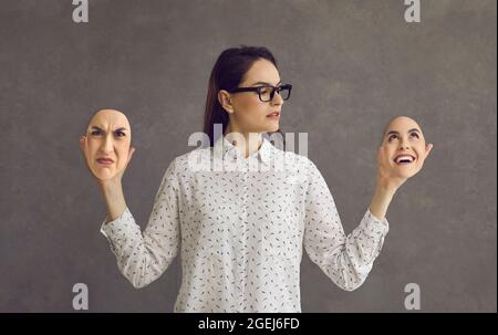 Junge Frau mit bipolarer Störung, die zwei Gesichtsmasken mit entgegengesetzten Emotionen hält Stockfoto