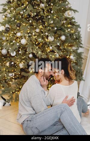 Junges hübsches Paar, das sich in der Nähe des Weihnachtsbaums zu Hause küsst. Stockfoto