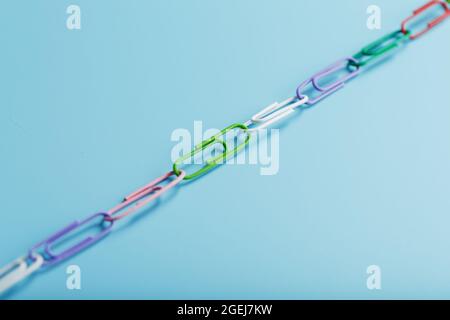 Eine Kette aus mehrfarbigen Büroklammern auf blauem Hintergrund. Geschäftskommunikation und Kooperationskonzept Stockfoto