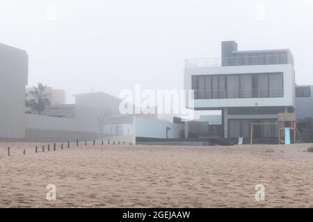 Außenansicht einer weißen und grauen modernen Villa an der Küste des Ozeans in einer luxuriösen Wohnanlage an einem nebligen Tag am Strand. Architekturhintergrund Stockfoto