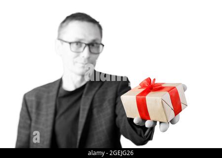 Porträt eines Mannes, der ein Geschenk in einer Hand hält, gebunden mit einem roten Band. Verschwommenes Schwarz-Weiß-Porträt und Farbgeschenk. Geringer Fokus. Stockfoto