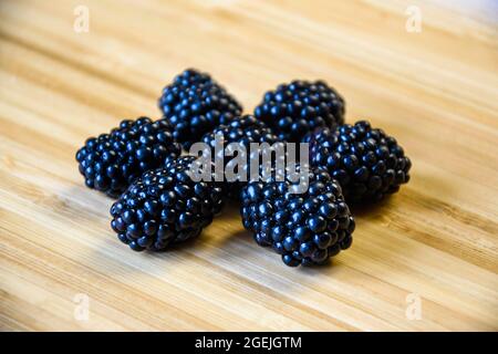 Sieben große reife Brombeeren in Form von Blume auf Holzhintergrund gelegt. Frische Beeren auf Bambusoberfläche, gesundes Lebensmittelkonzept. Nahaufnahme Stockfoto