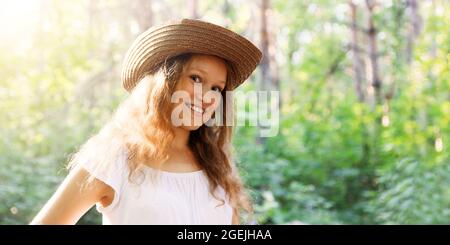 Nahaufnahme Porträt eines jungen Langhaar-Mädchens in einem Strohhut in hellem Sonnenlicht vor verschwommenem Naturhintergrund. Copyspace. Stockfoto