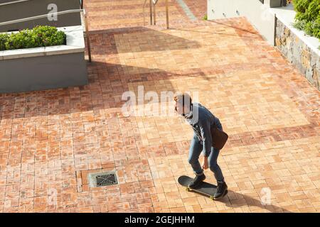 Ernst kaukasischen männlichen Unternehmen kreative Ankunft auf Skateboard außerhalb des Arbeitsplatzes Stockfoto