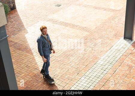 Ernst kaukasischen männlichen Unternehmen kreative Ankunft auf Skateboard außerhalb des Arbeitsplatzes Stockfoto