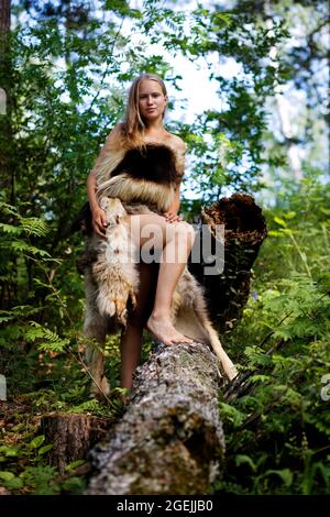 Wildes Mädchen in Tierfellen unter den Bäumen im Wald gekleidet. Geringer Fokus. Stockfoto