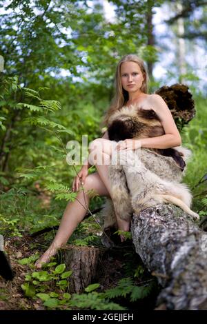 Wildes Mädchen in Tierfellen unter den Bäumen im Wald gekleidet. Geringer Fokus. Stockfoto