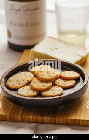 Käsekekse oder Cracker auf einem Teller mit Käse und einem Glas Weißwein Stockfoto