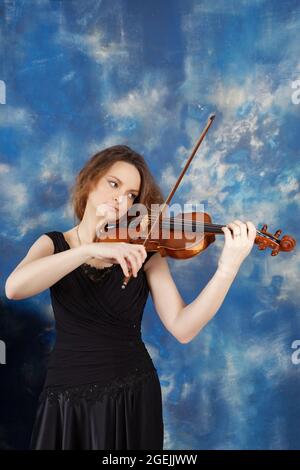 Junge Frau spielt Geige vor abstrakt blauem Hintergrund. Stockfoto