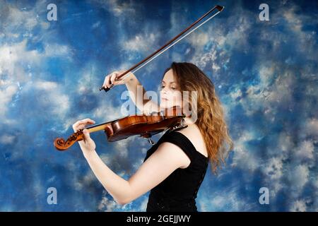 Junge Frau spielt Geige vor abstrakt blauem Hintergrund. Stockfoto